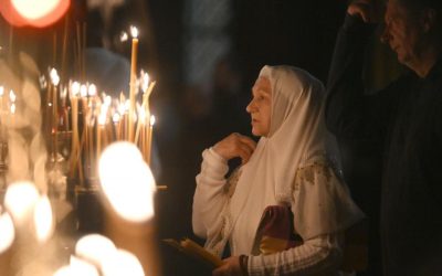 femeie care se roaga in biserica in apropierea unor lumanari